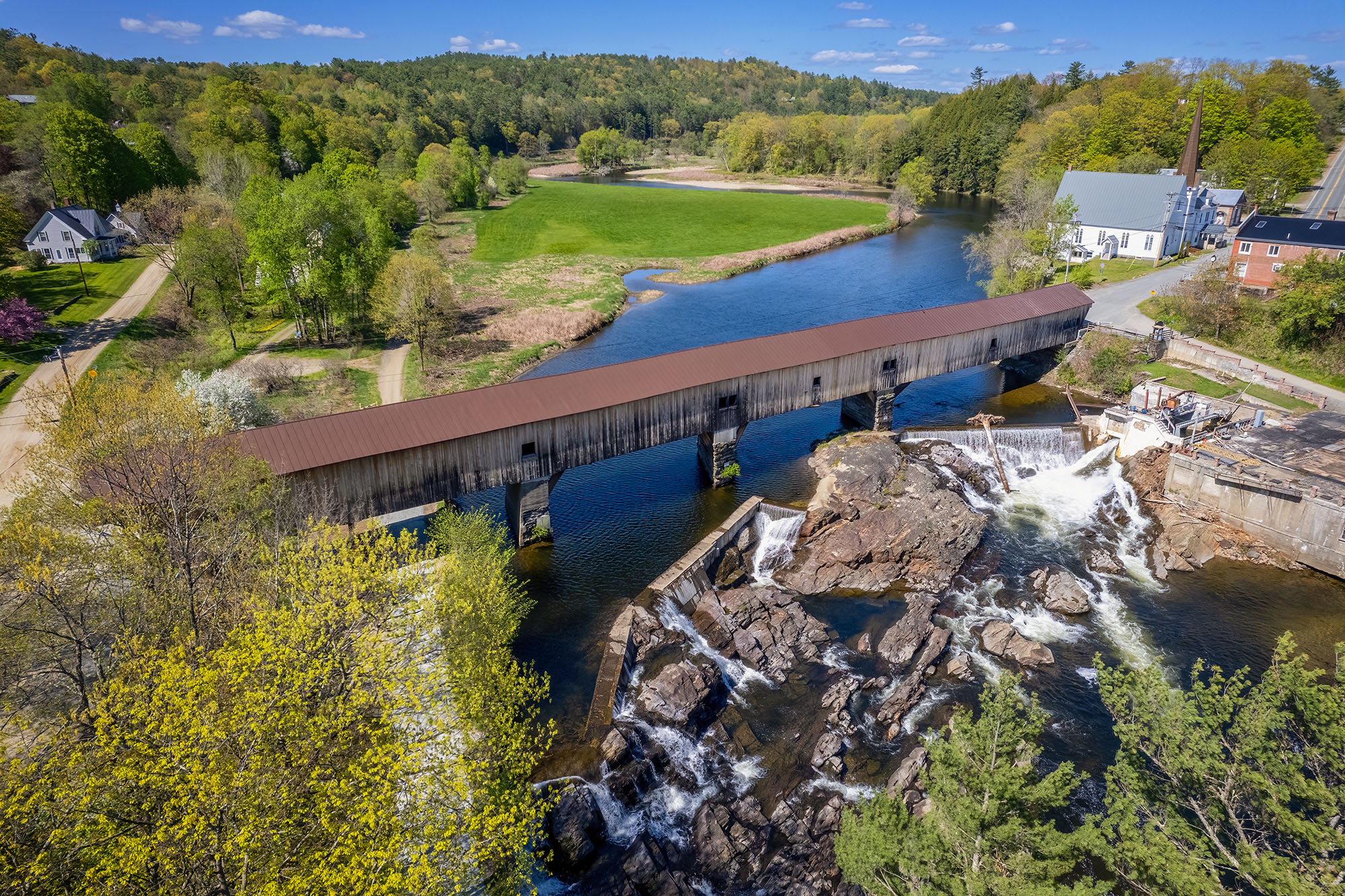 Bath Covered Bridge and the Cascading River This aerial view, captured by a drone, presents the entirety of the Bath Covered Bridge in New Hampshire. The bridge gracefully...