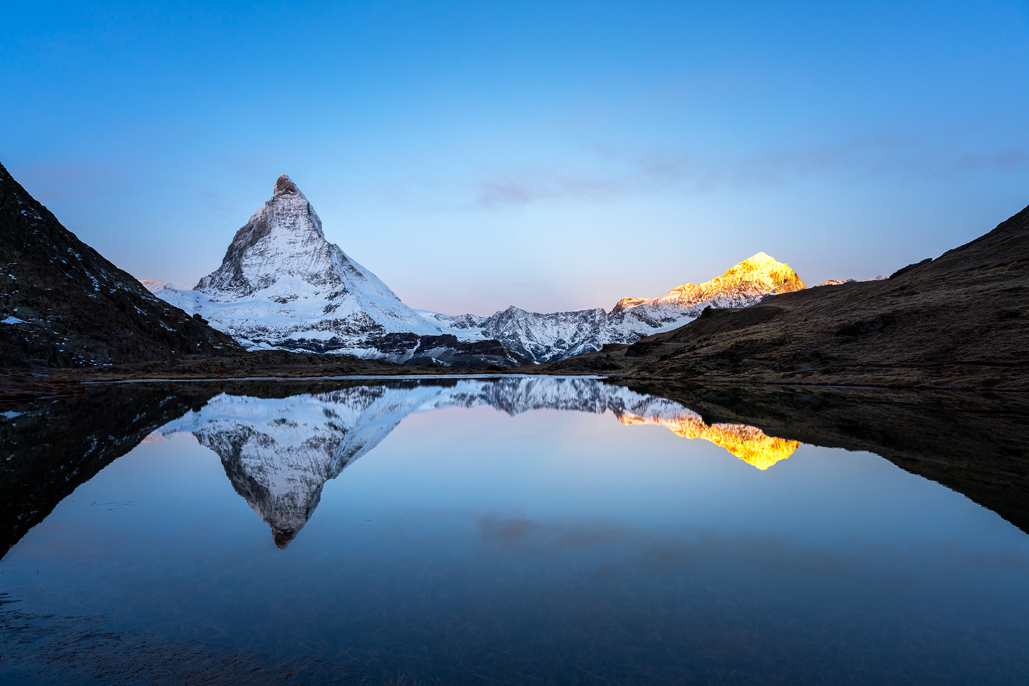 In "Matterhorn's Dawn Reflection," the moment just before sunrise bathes the Swiss landscape in a gentle transition from blue...