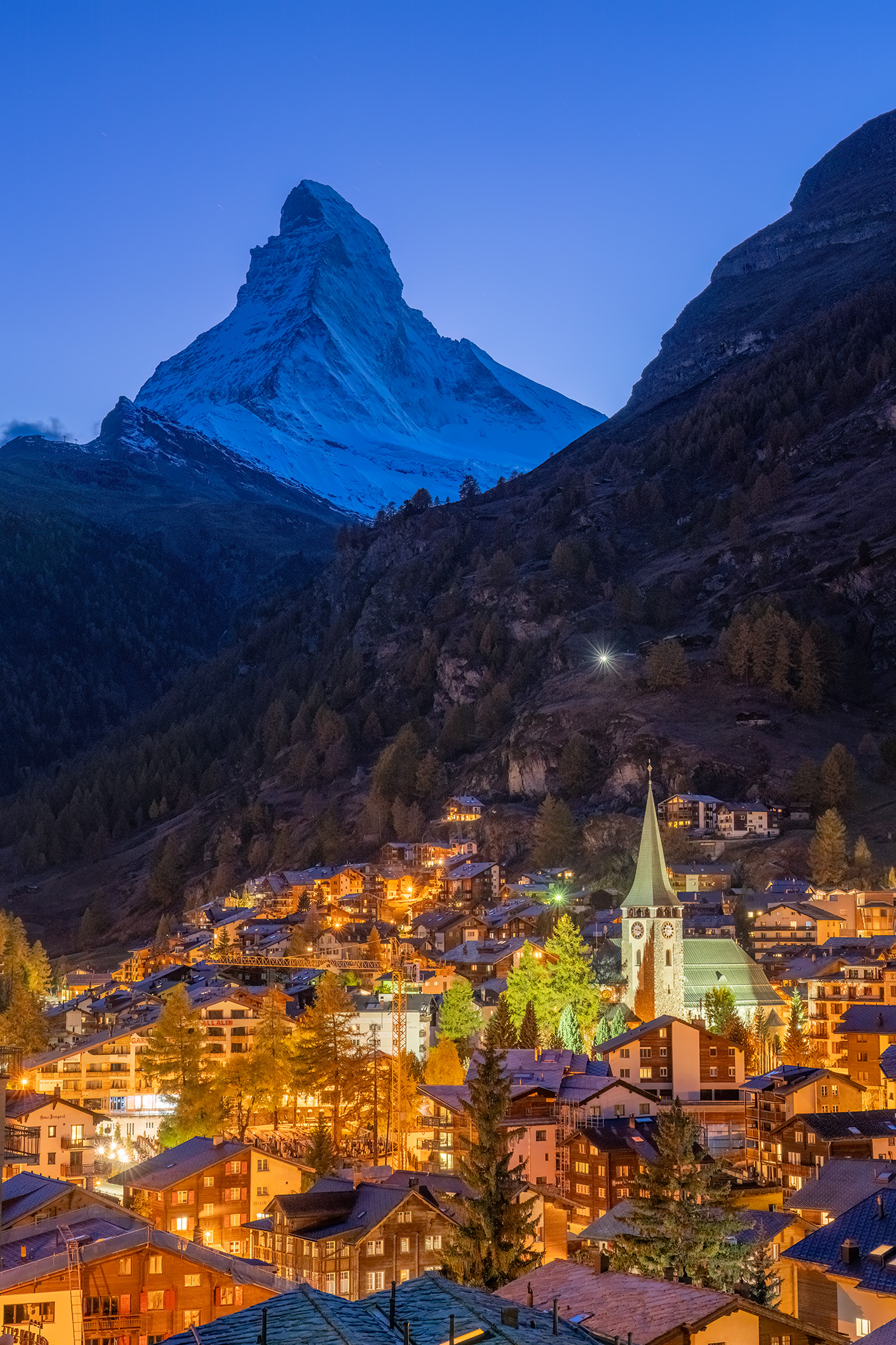 In "Zermatt's Twilight Embrace," the iconic Matterhorn watches over the warmly lit village during the blue hour in Switzerland...