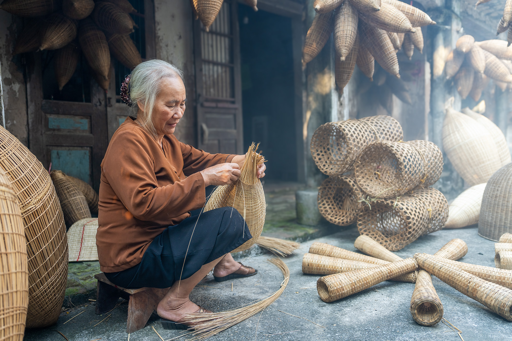 Crafting Nets in Hazy Light This image captures a woman meticulously weaving fish nets in a workshop near Hanoi, Vietnam. Her hands work skillfully on a...