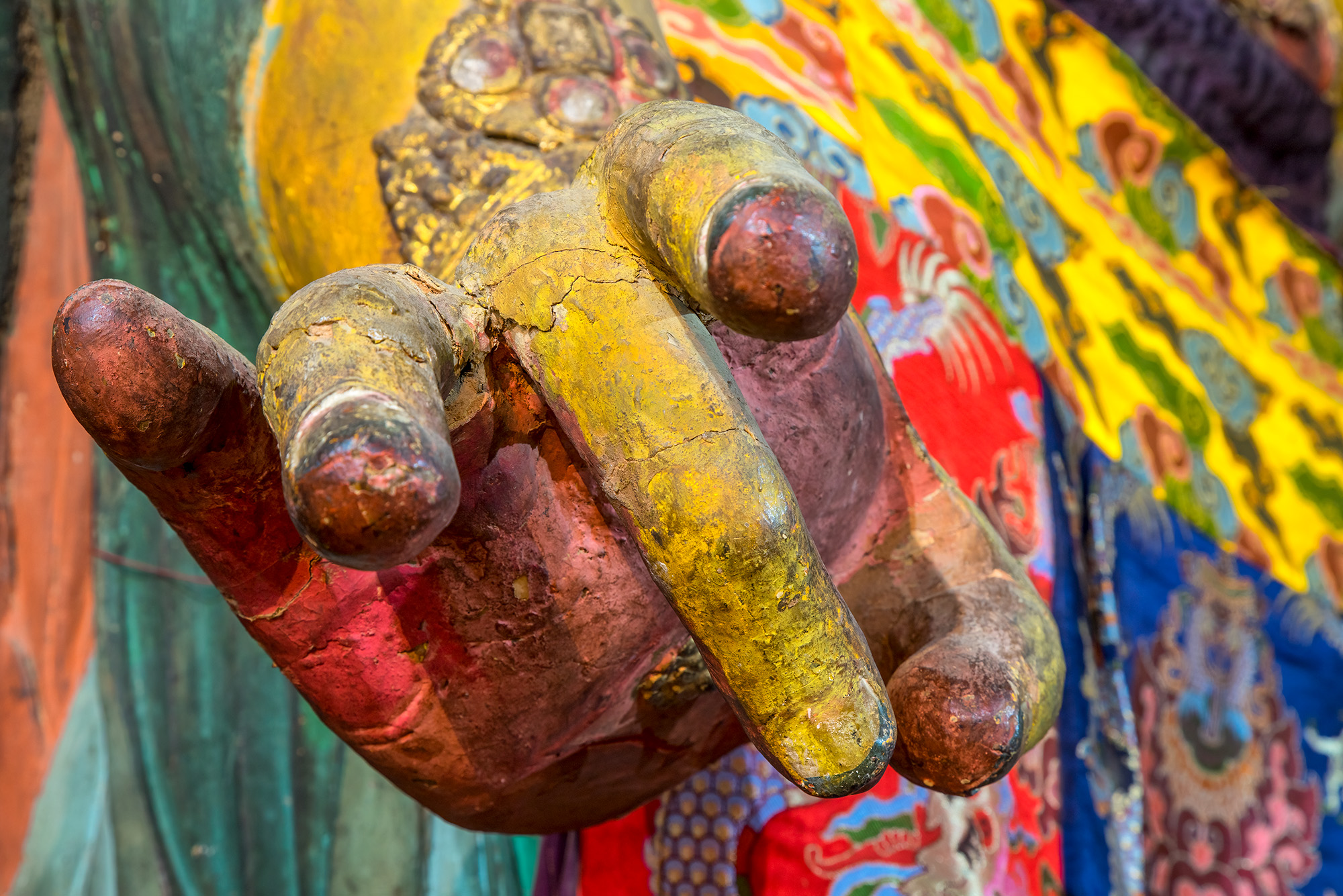 "Buddha's Multicolored Mudra" offers a close-up view of a hand from one of the vibrant, multi-colored Buddhist statues found...