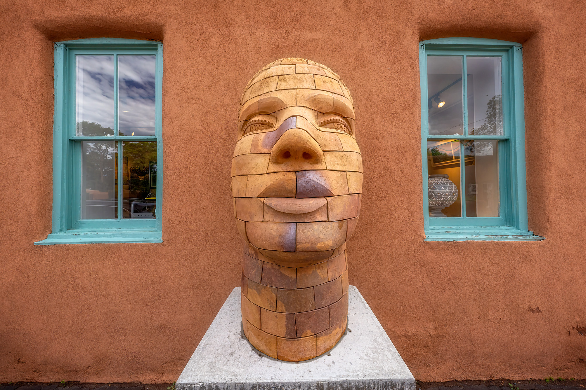 This image, captured in Santa Fe's vibrant art district, portrays an adobe wall adorned with two windows trimmed in refreshing...