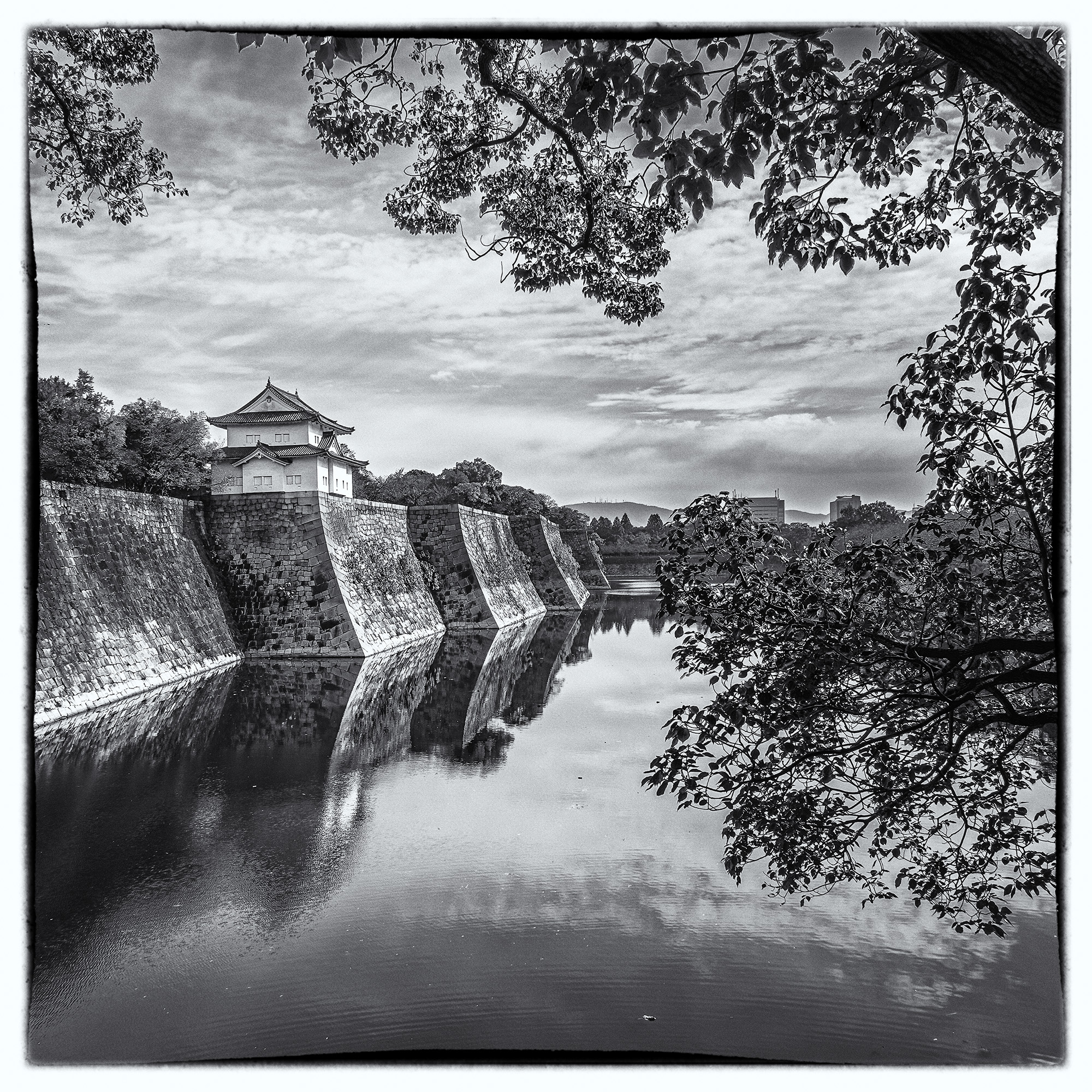 In a square frame, "Osaka Castle's Reflective Embrace" reveals an enchanting black-and-white dreamscape. A guard tower, nestled...
