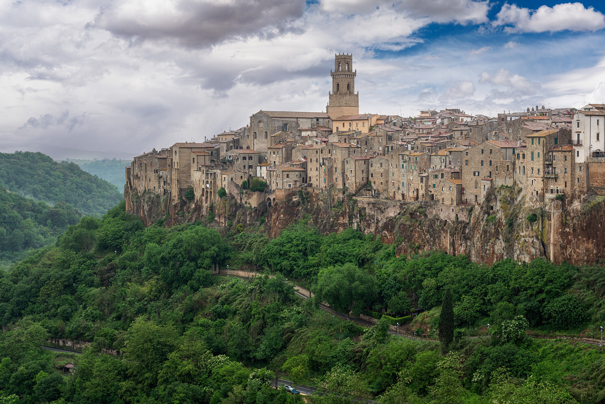 From a distance, a photograph reveals the medieval town of Pitigliano, with tightly constructed buildings rising high above the...