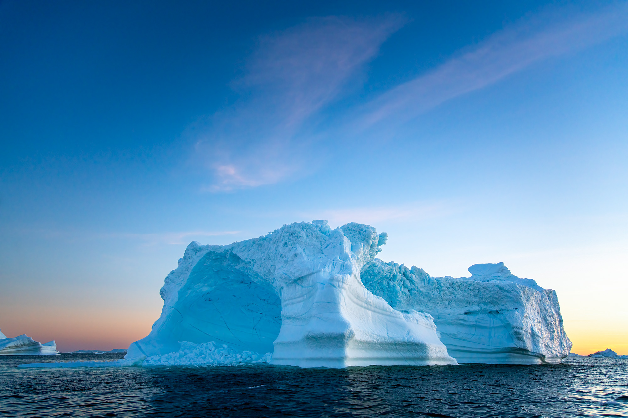 In this image, taken at 1:30 AM, the setting sun hovers on the horizon, casting its ethereal glow over an iceberg floating serenely...