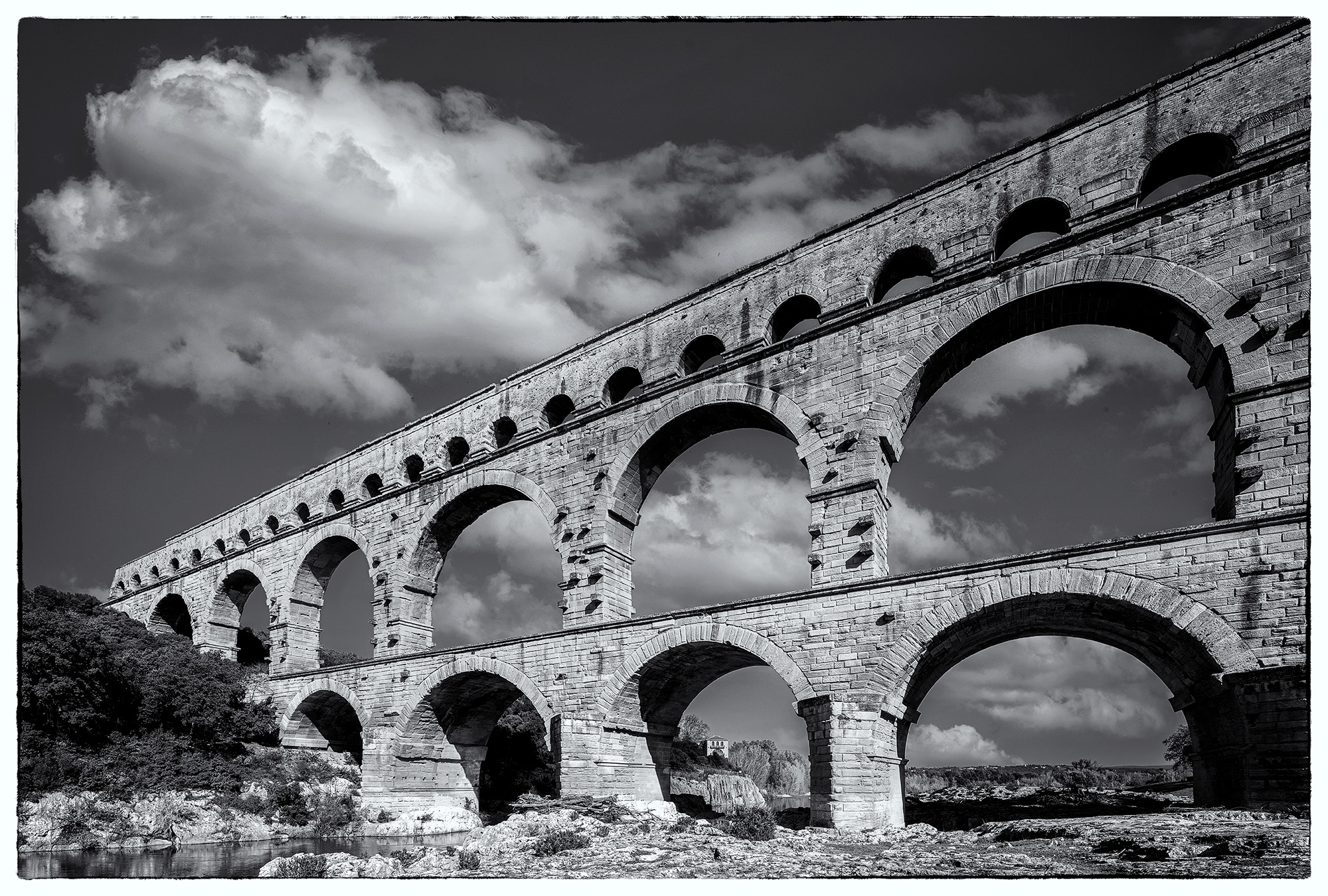 This Black & White image, taken at Pont du Gard, France, captures the awe-inspiring Roman aqueduct that has defied time and stands...