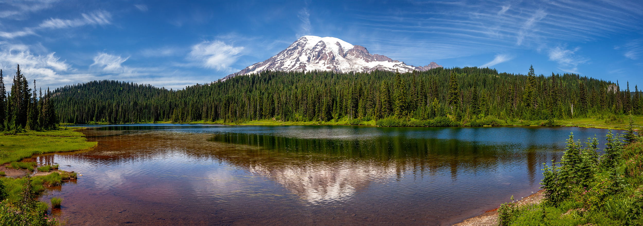 Mount Rainier's Mirror This panoramic image, captured in Mount Rainier National Park, unveils the mountain's grandeur as it reflects in a tranquil pool...