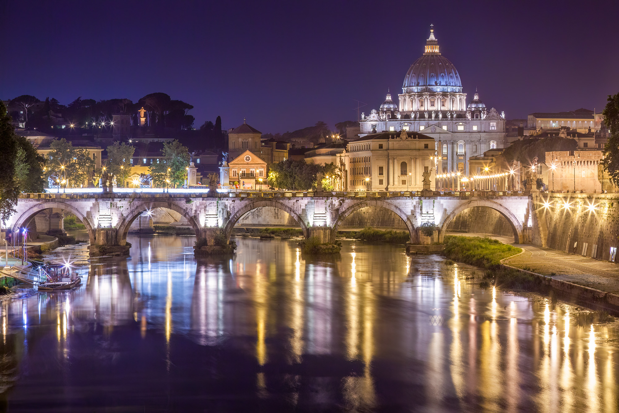 In this nocturnal vista of the Vatican from Rome, the St. Angelo Bridge spans the tranquil Tiber River. Gazing towards the Vatican...