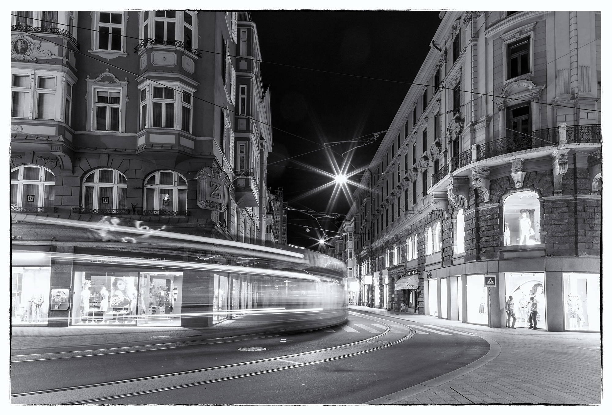 Night Motion in Innsbruck This black & white photograph captures the lively atmosphere of Innsbruck, Austria, at night. A tram gracefully curves to the...