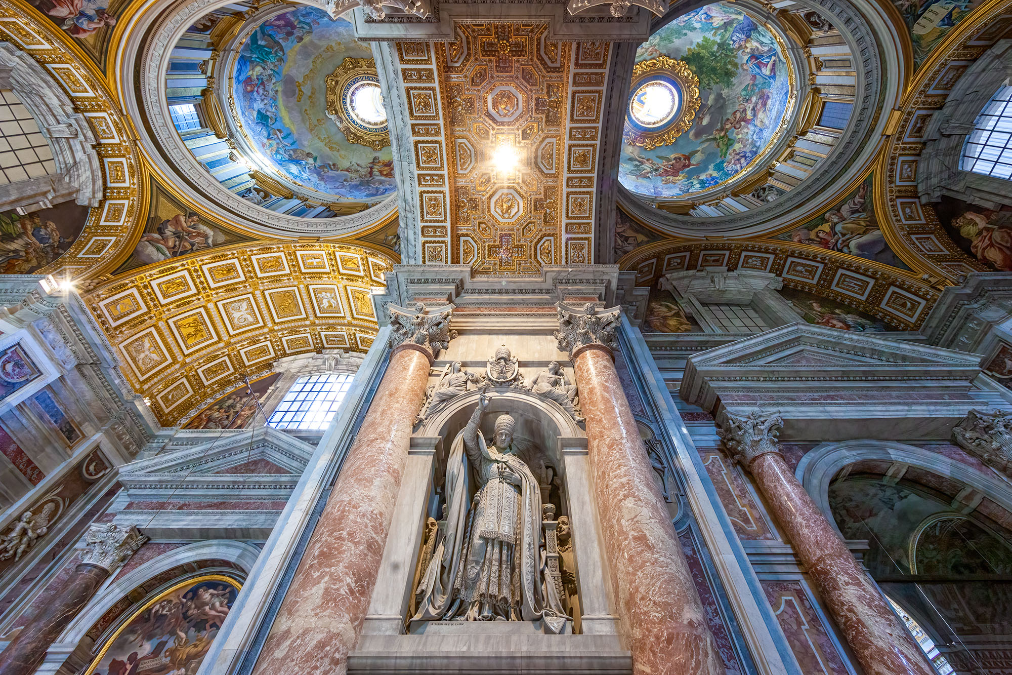 Pope Pius X and the Heavenly Canvases In this image, a sculpture of Pope Pius X rises majestically on a central pillar, drawing the eye upward to a stunning ceiling...