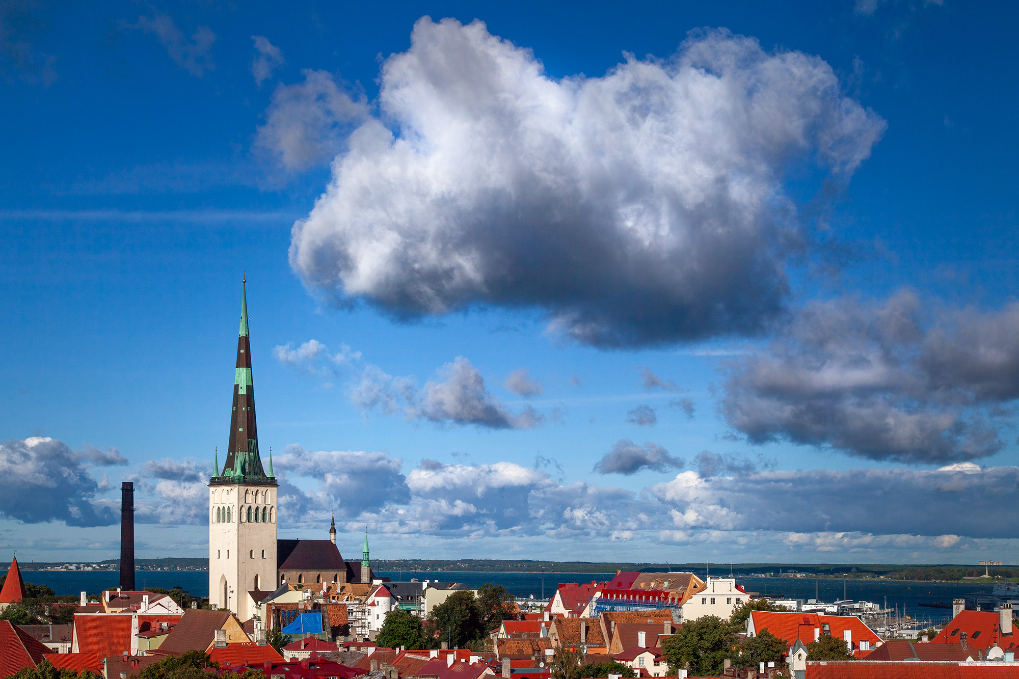 In this striking image captured in Tallinn, Estonia, the iconic St. Olaf's Church steeple rises proudly above a sea of rooftops...