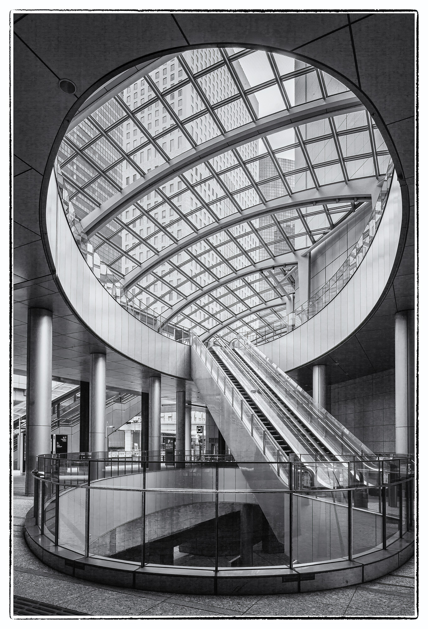 This black and white image, captured in Tokyo, Japan, within Shiodome Station, offers a unique perspective. A circular opening...