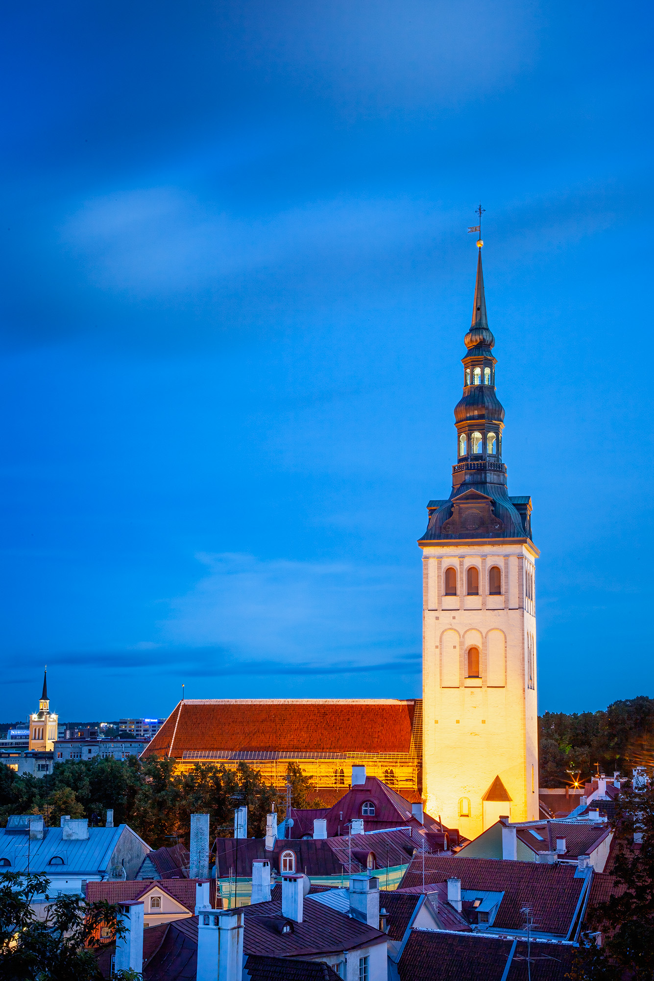 St. Olaf's Illumination Amidst Tallinn's Twilight This vertical image, taken during the enchanting blue hour in Tallinn, Estonia, highlights the radiant St. Olaf's Church amidst...