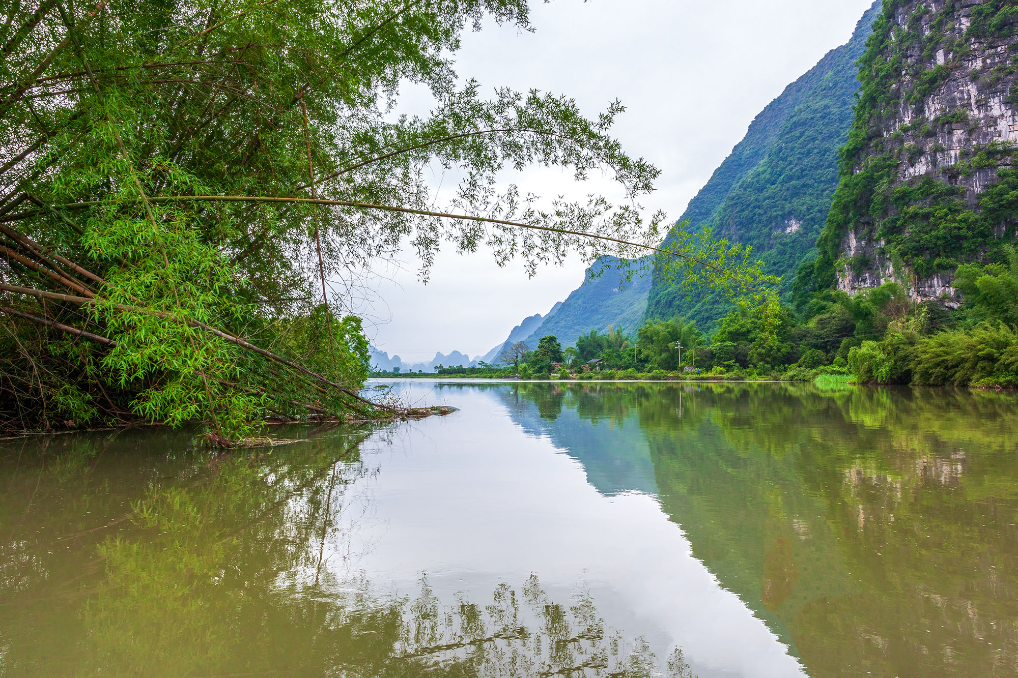 On a traditional raft along the Li River, this image captures a serene moment. Towering mountains and lush bamboo groves are...