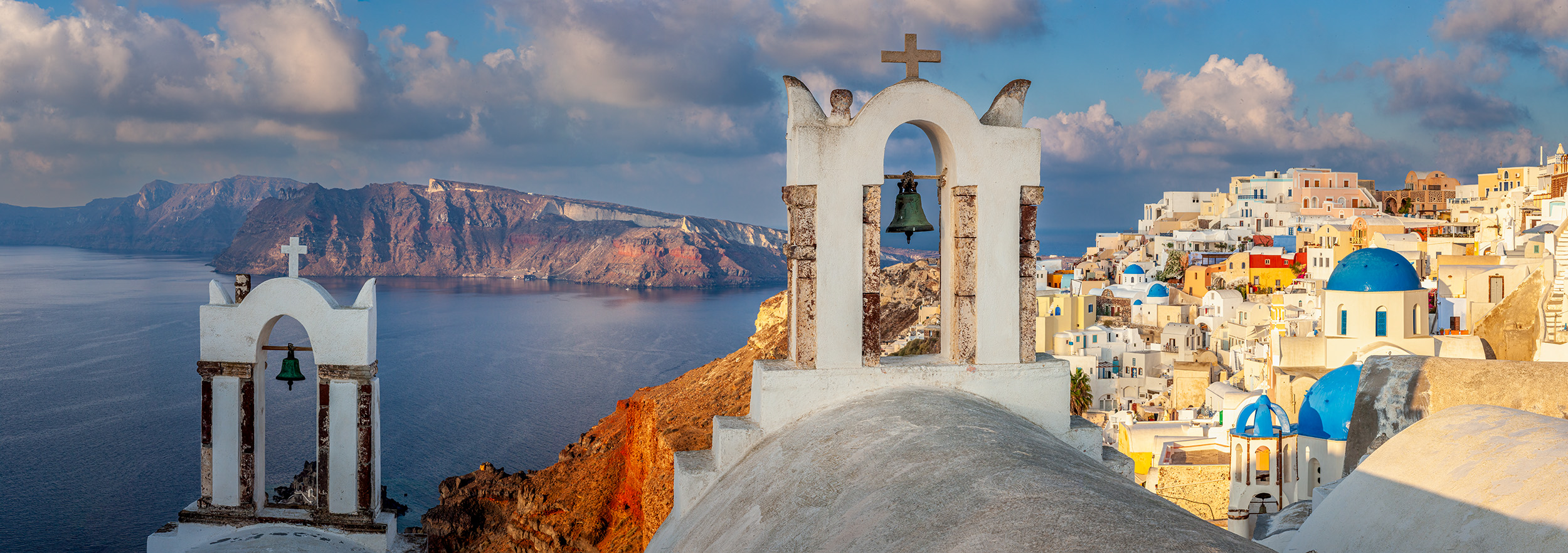 Oia's Coastal Watch This panoramic image captures the essence of Oia, Santorini, Greece. In the foreground, two church belltowers stand tall, symbolizing...
