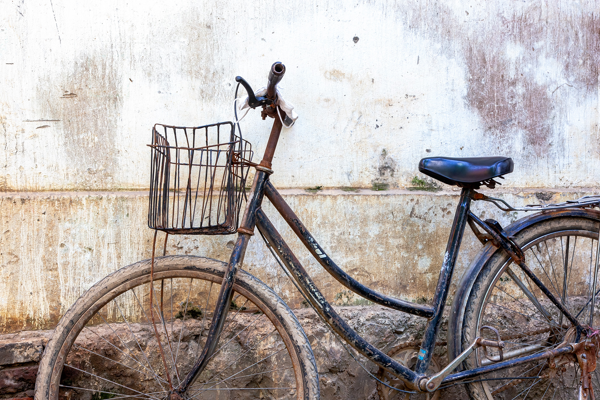 Yangshuo's Well-Worn Bicycle In this image from Yangshuo, China, a weathered bicycle and its trusty basket lean against a slightly soiled white wall. The...