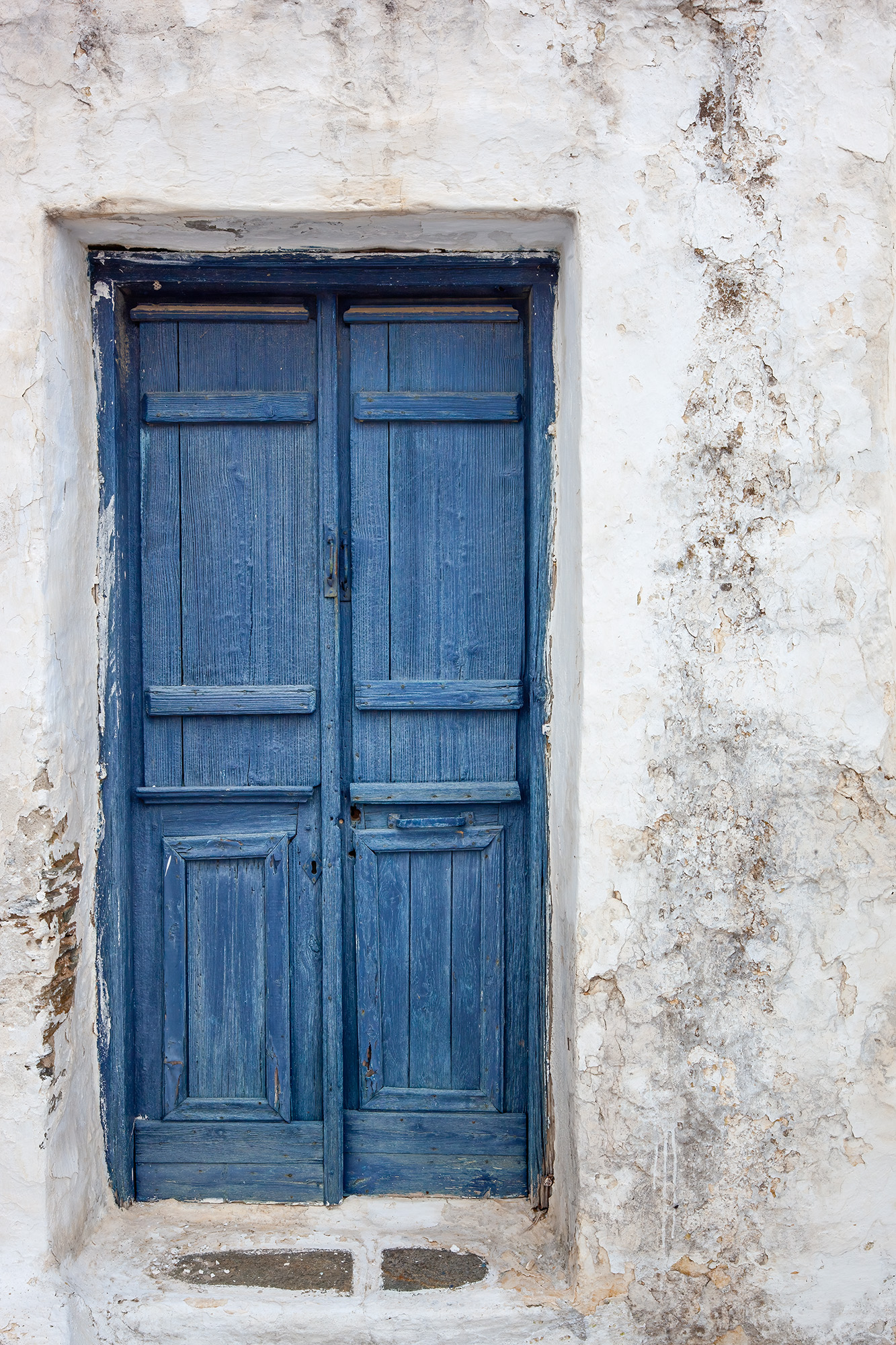 In this striking vertical composition, we encounter a beautifully weathered blue door set within the rugged charm of Sifnos...