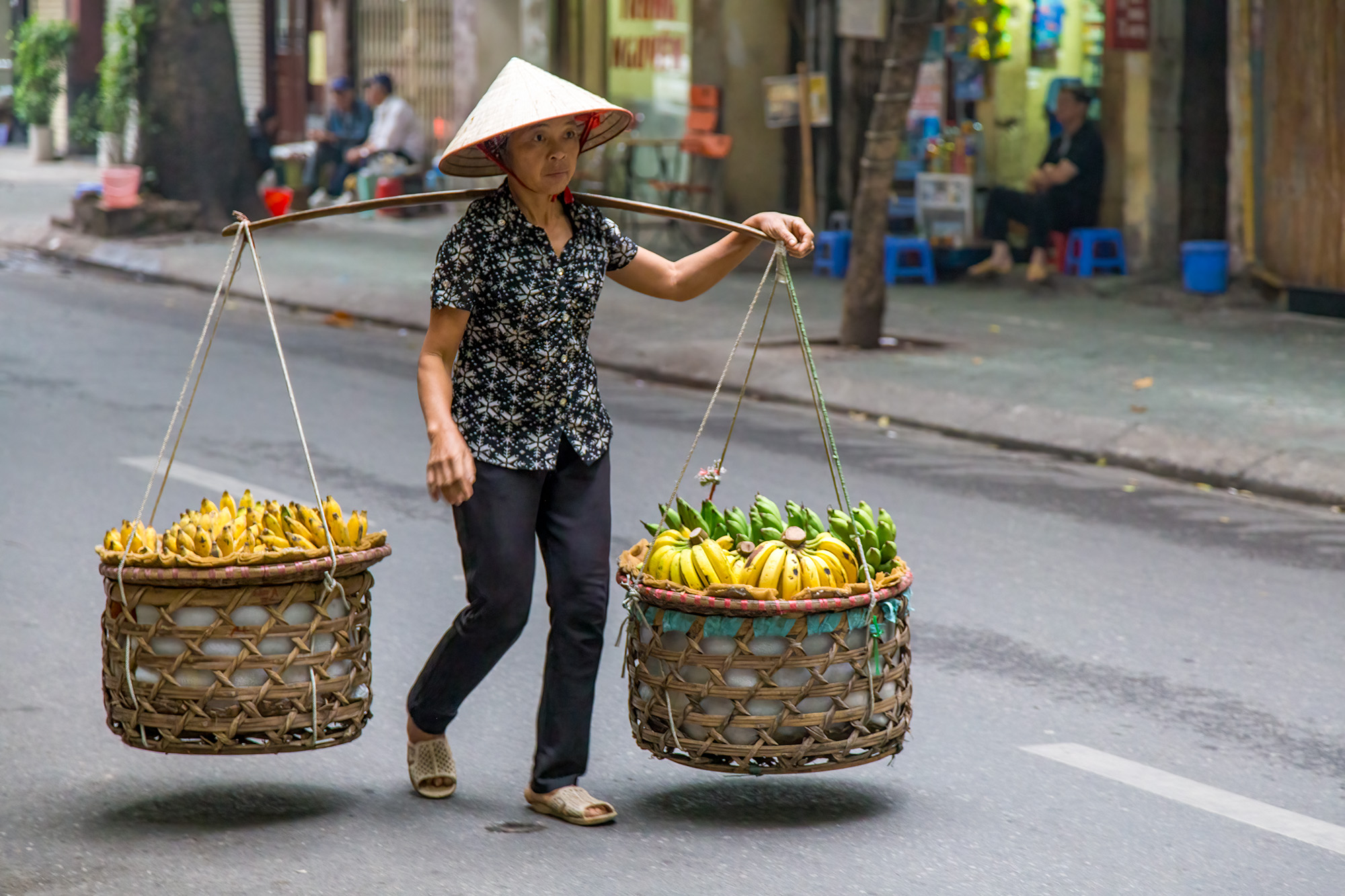 In the bustling streets of Hanoi, Vietnam, a hardworking street vendor carries the weight of her livelihood with unwavering determination...