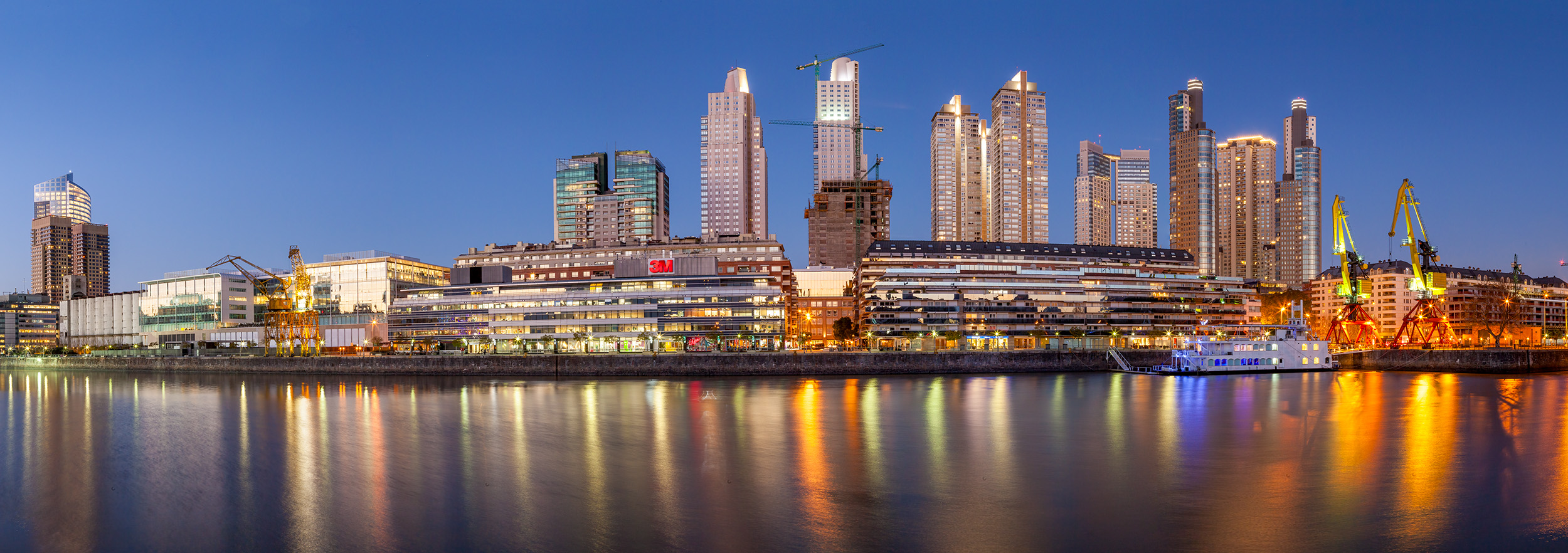 This photograph, captured in Buenos Aires, Argentina, presents a panoramic view of Puerto Madero during the serene blue hour....