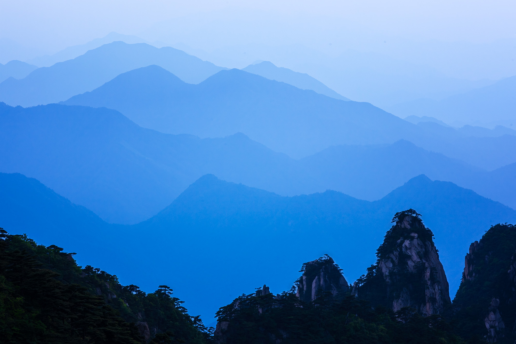 This image, from Mount Huangshan in China, unveils an enigmatic landscape. Against a misty blue sky, only the outlines of several...