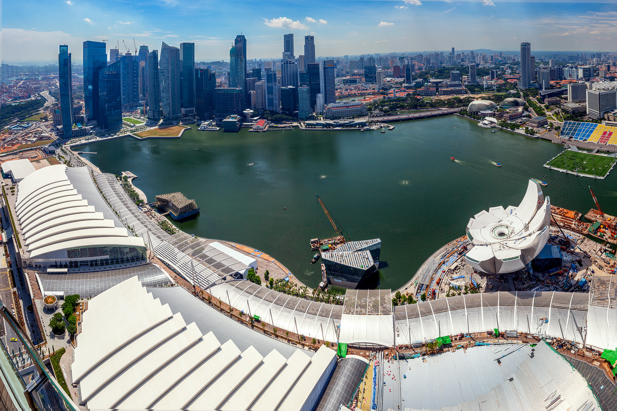 This image captures the expansive view from the top of the Marina Bay Sands Hotel, showcasing the broad cityscape and foreground...