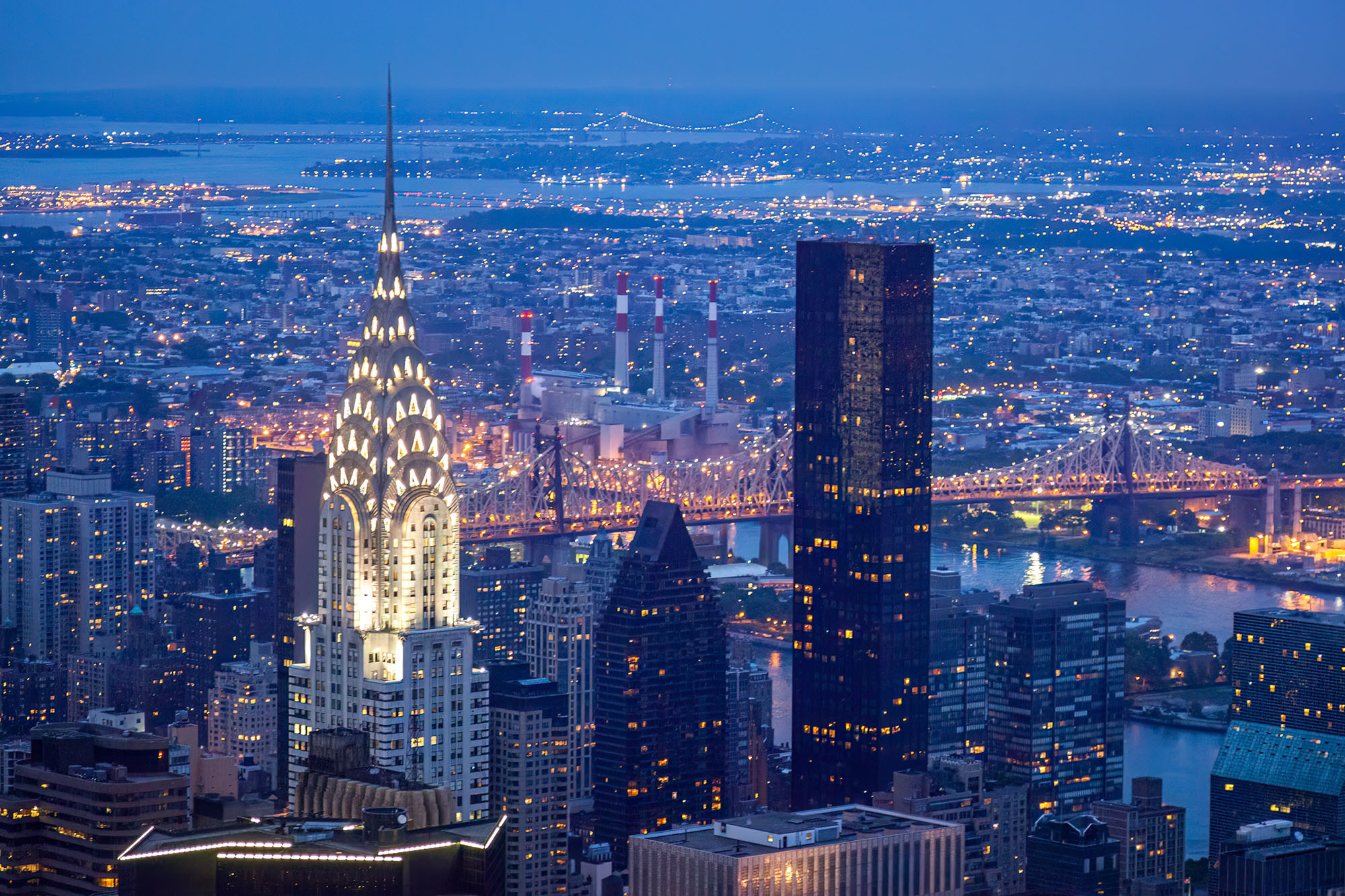 This image, captured from the Empire State Building's summit during the serene blue hour, showcases the iconic Chrysler Building...