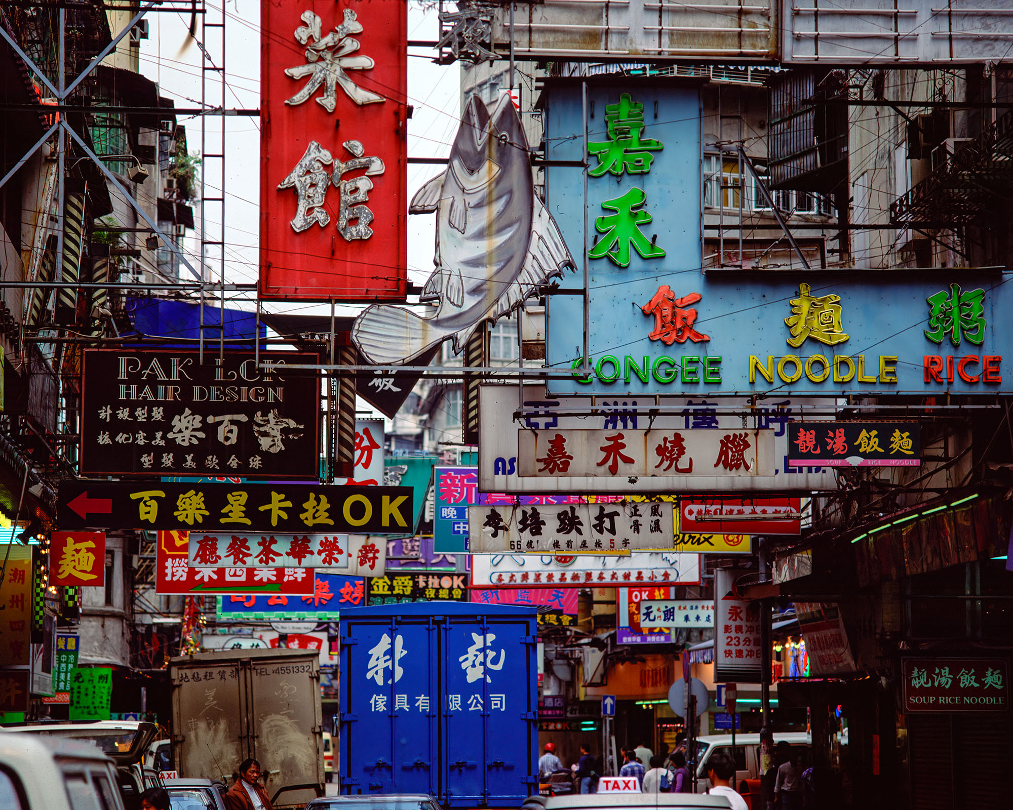 Captured with my Bronica ETRSi camera, this image showcases a vibrant tapestry of colorful signs adorning the buildings in bustling...